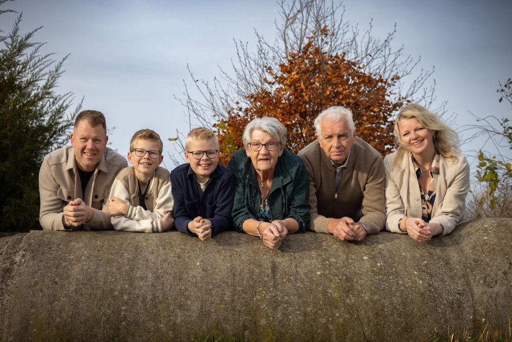 Multi-generational group posing together while leaning on a stone wall outdoors.