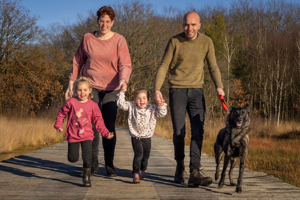 A family walks together with their black dog on a pathway through autumn fields.