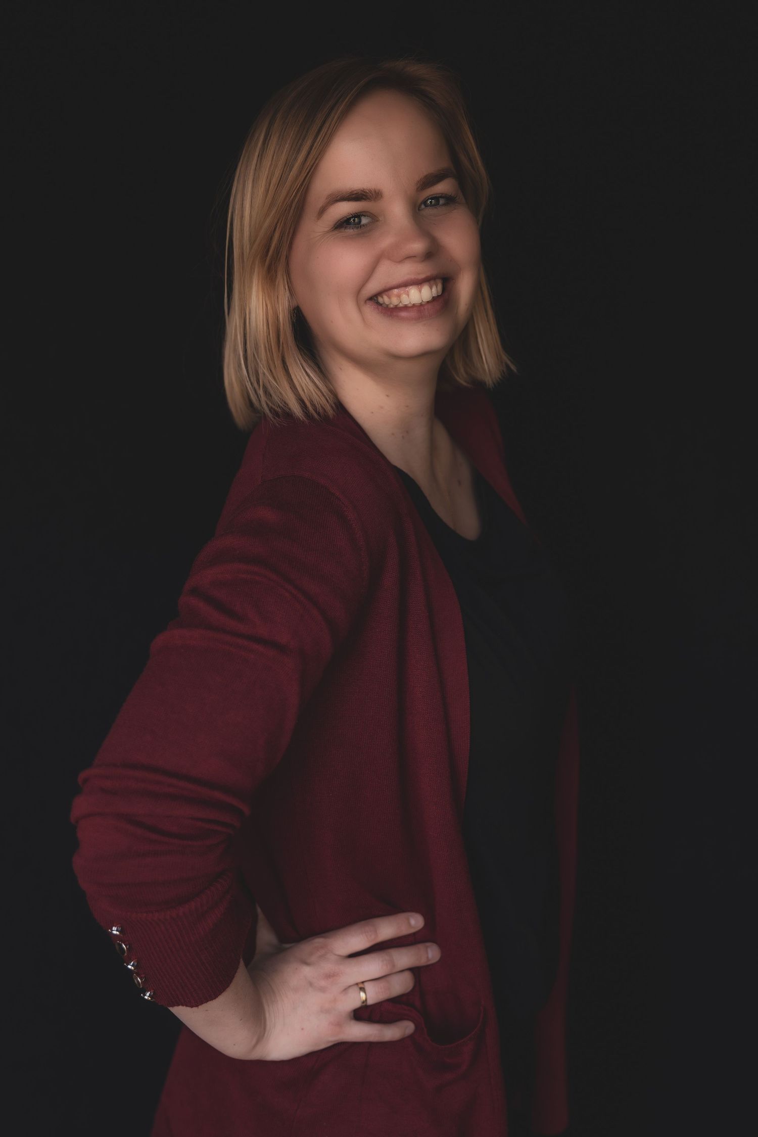 Professional portrait against dark background showing bright smile and burgundy blazer in dramatic lighting.