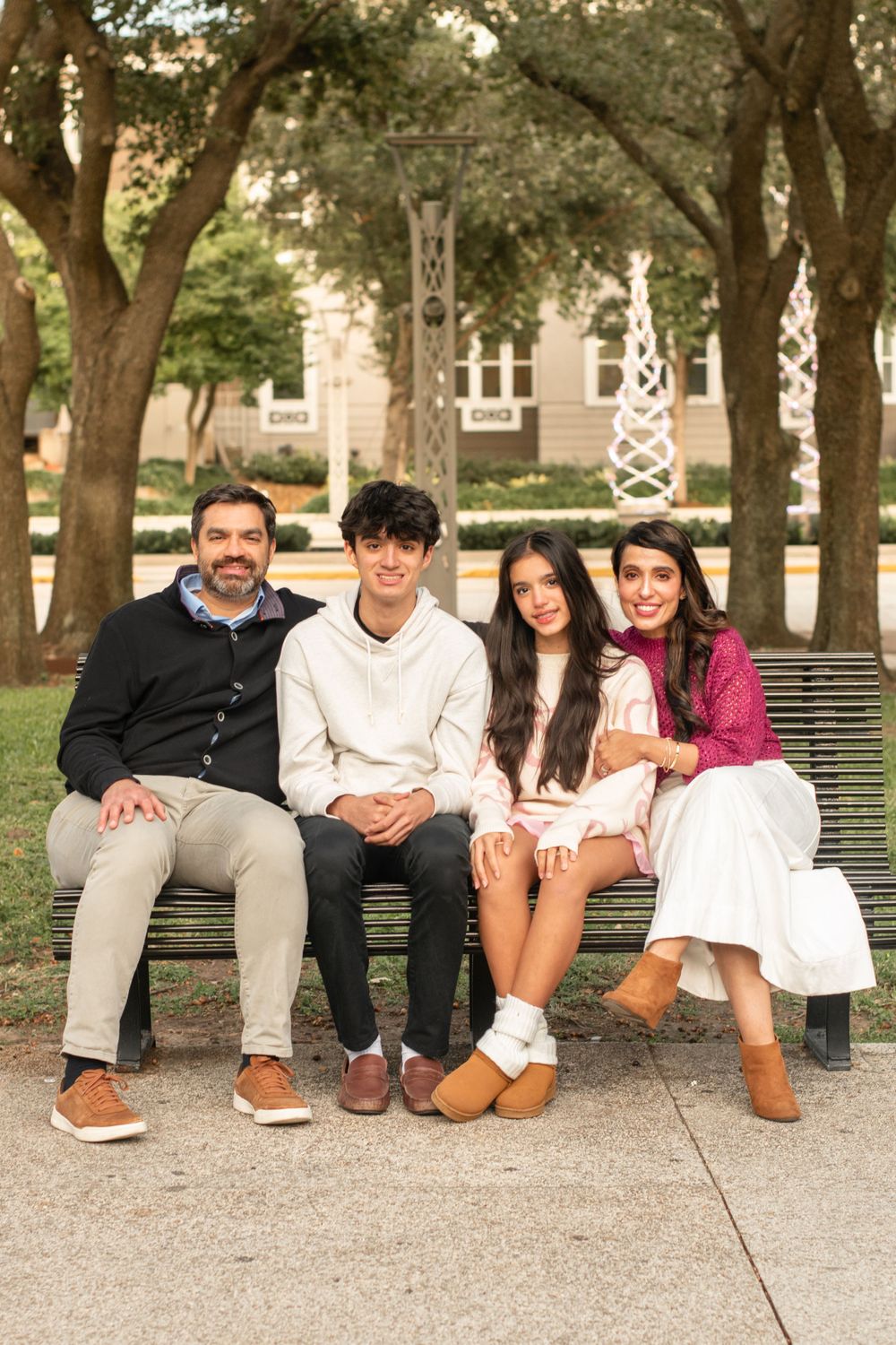 Group sitting together on park bench surrounded by trees in casual attire.