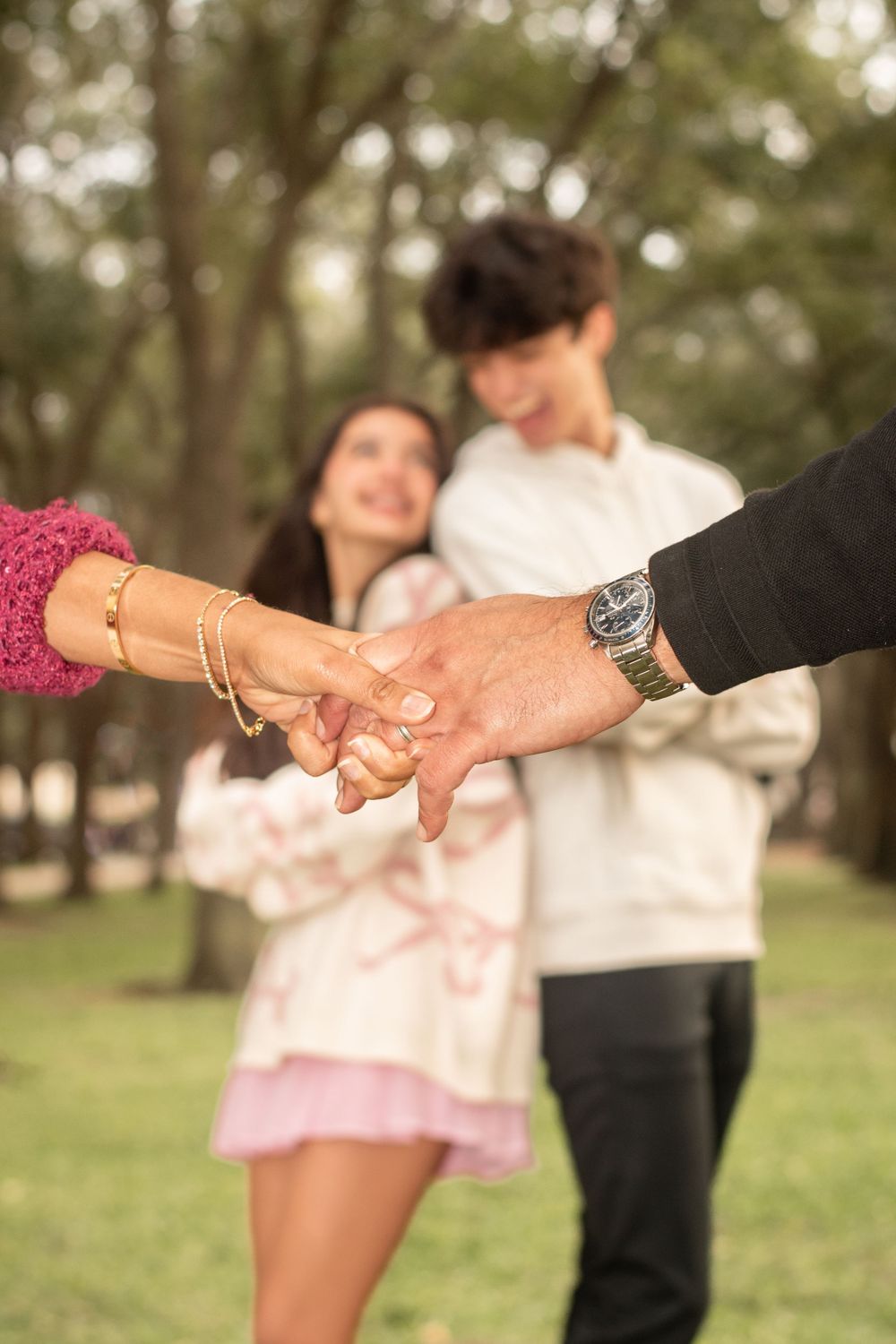 Close-up of hands holding while couple stands in background at park during romantic outdoor photo shoot.