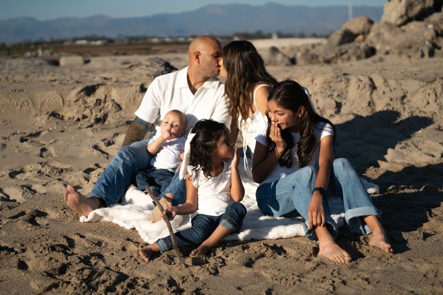 Family relaxing together on a rocky beach during golden hour.