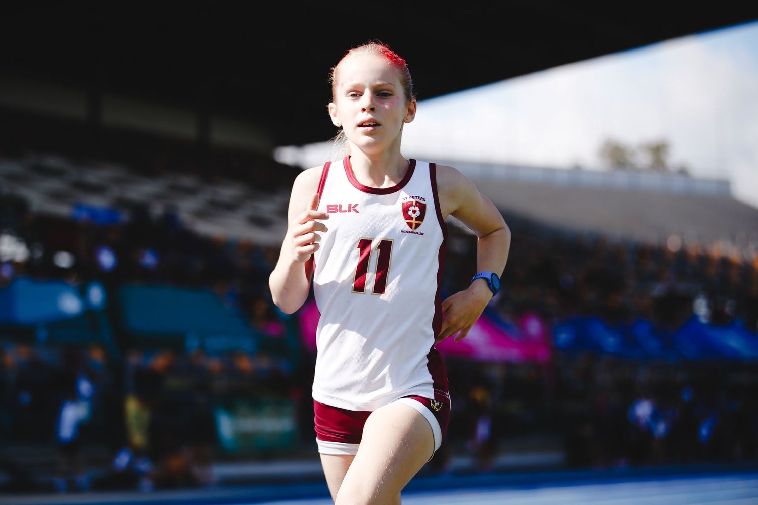 Athlete in white jersey running during competitive track and field event.