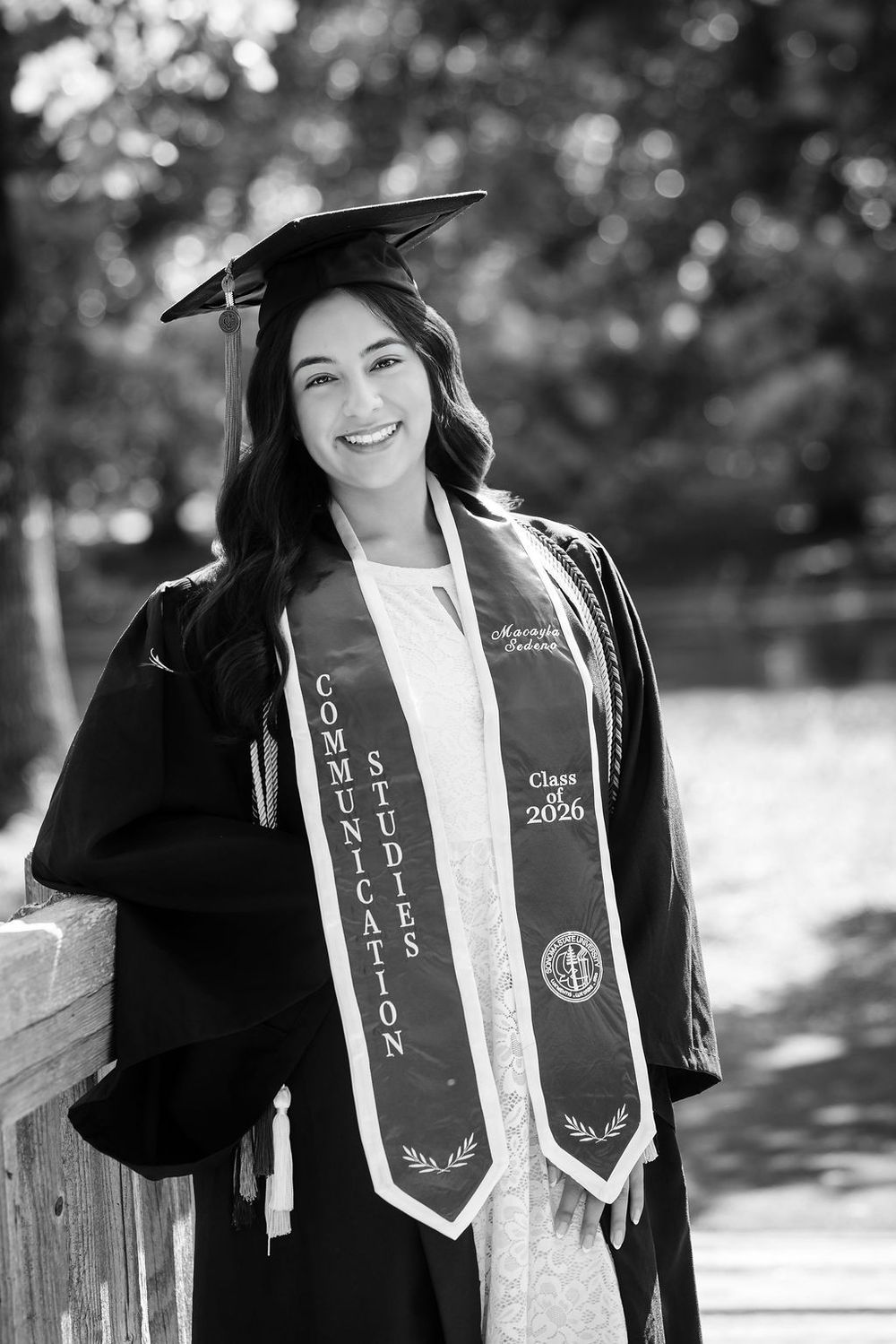 Black and white photo of smiling graduate in cap and Communication Studies stole, Class of 2026.