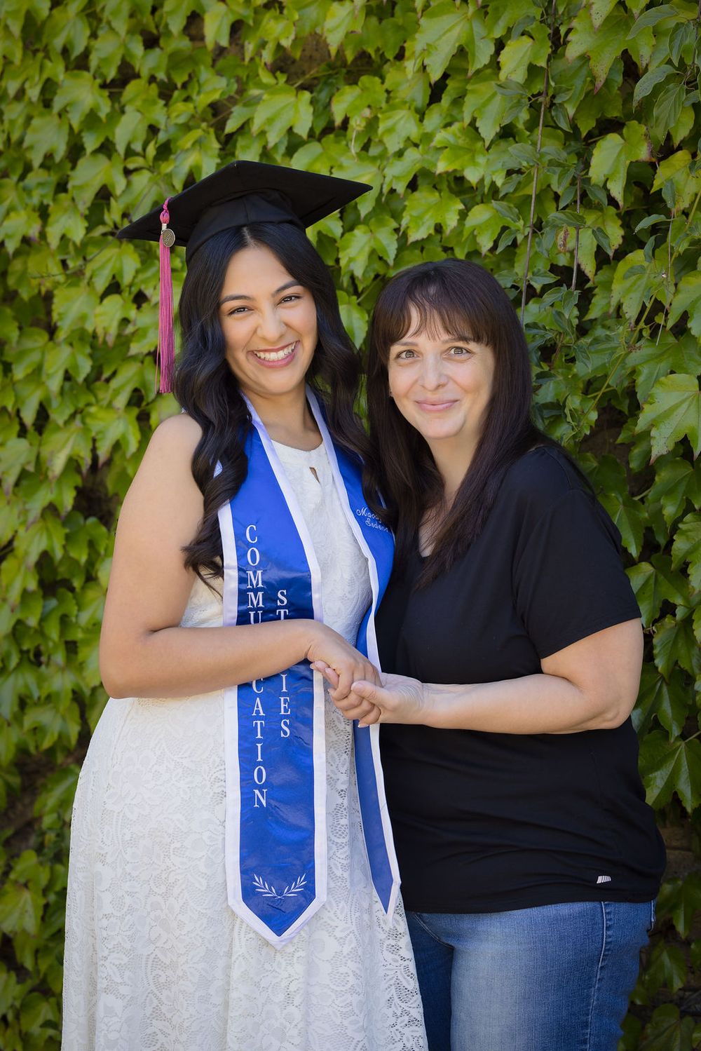 Graduate in cap and blue stole smiles with older woman in front of ivy-covered wall.