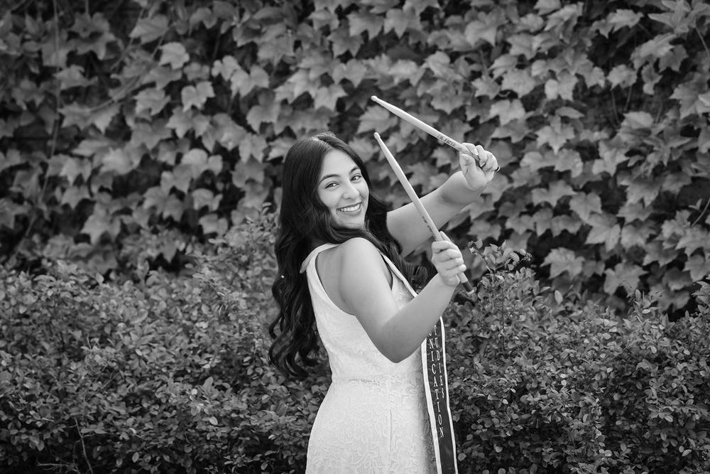 Young woman smiling and playing violin outdoors in black and white photo with ivy wall background.