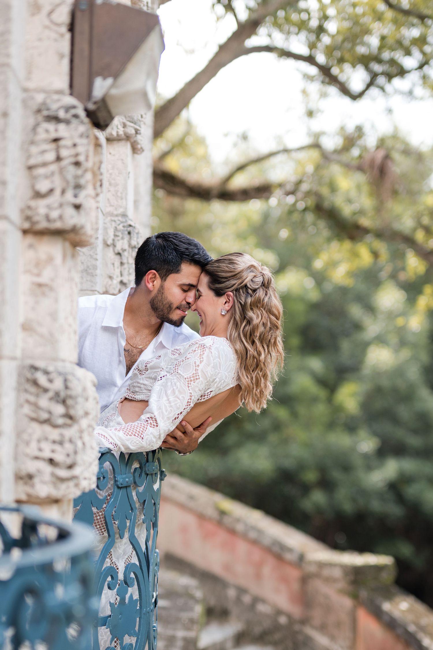 Bride and groom share a joyful embrace on a historic balcony at Vizcaya Gardens, surrounded by lush greenery and stone architecture.