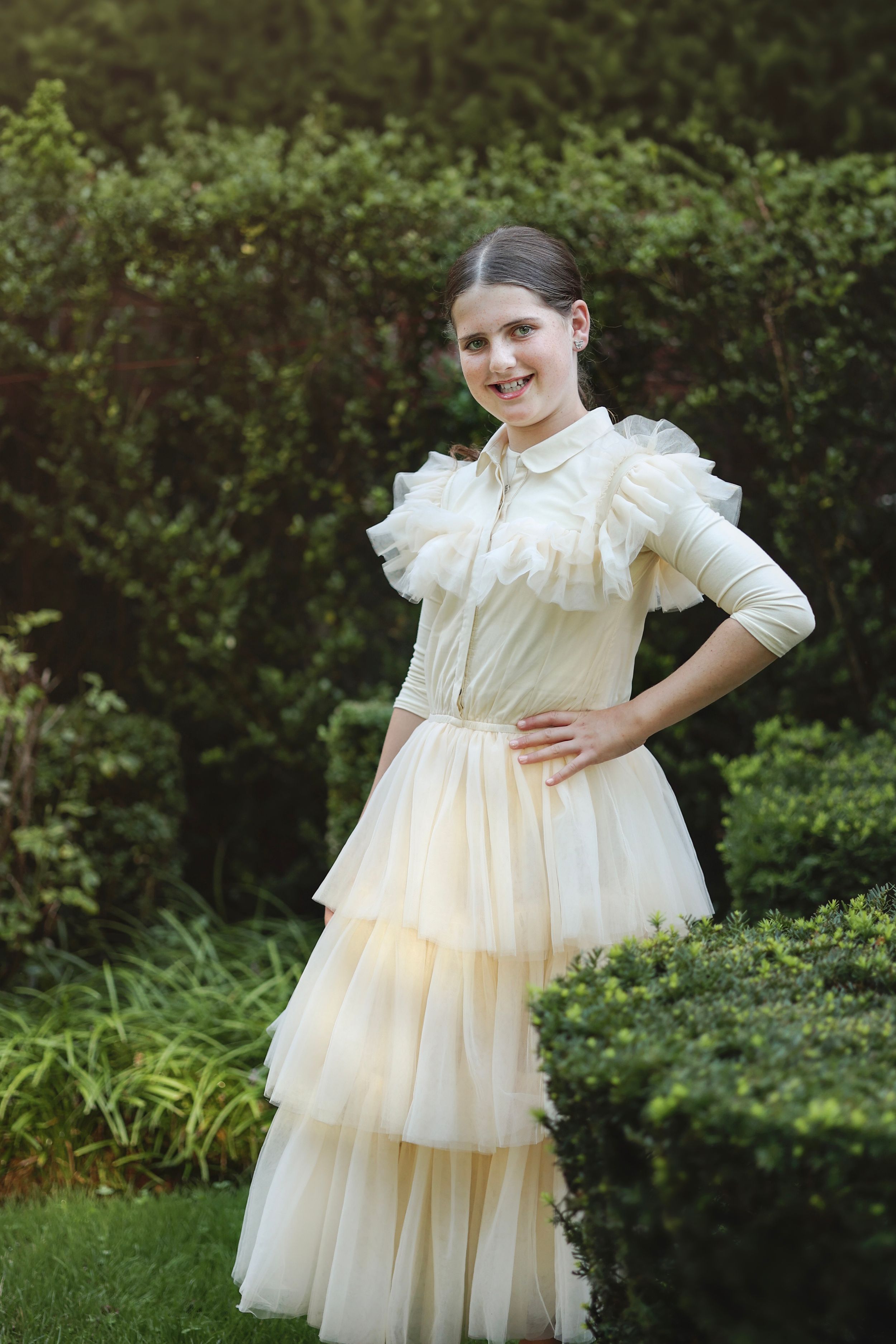Portrait of a bas mitzvah girl wearing a ruffled gown posing in her home yard