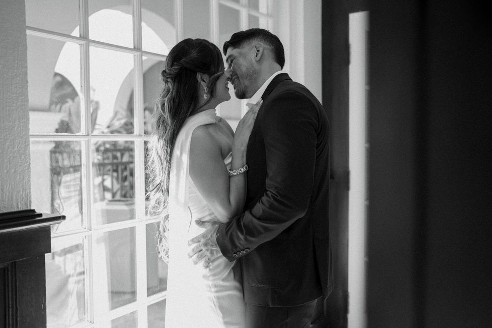 A couple shares an intimate moment by French doors in a black and white wedding photo.