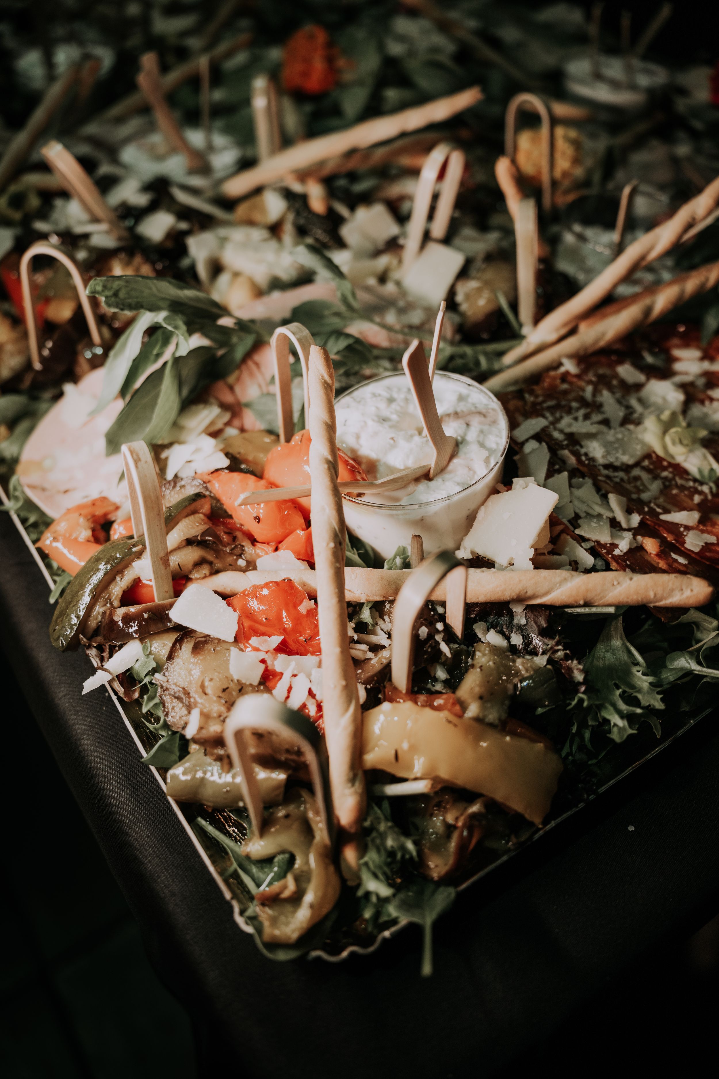 Elegant wedding charcuterie board with breadsticks, fresh vegetables, dipping sauce, and greens arranged on a decorative platter.