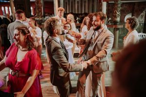Two grooms share a joyful dance together at their wedding reception surrounded by celebrating guests.