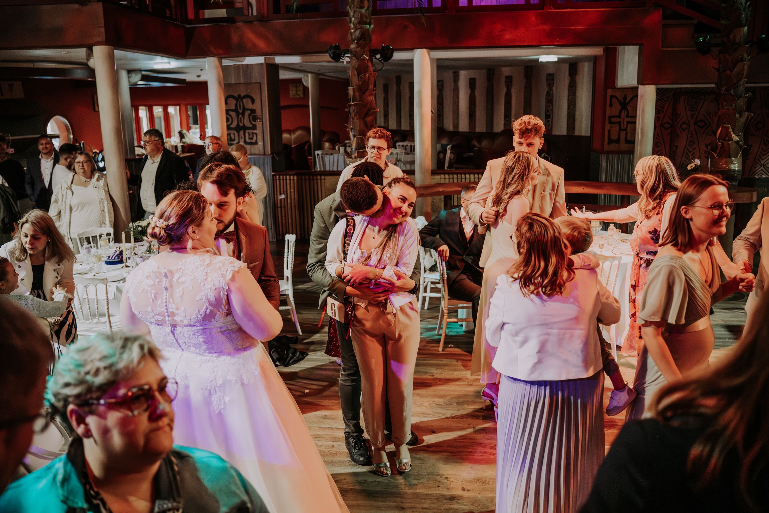 Guests dancing and celebrating at a lively indoor wedding reception with colorful lighting.