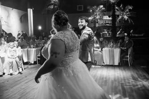 Bride and groom share first dance at wedding reception in black and white photo with guests watching.