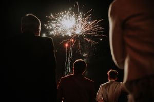 Group of people watching colorful fireworks exploding in dark night sky at an outdoor celebration event.