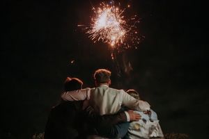 Group of friends hugging while watching colorful fireworks burst in the night sky.
