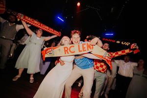 Excited wedding guests celebrate on a dance floor holding RC Lens football scarves at a lively reception party.