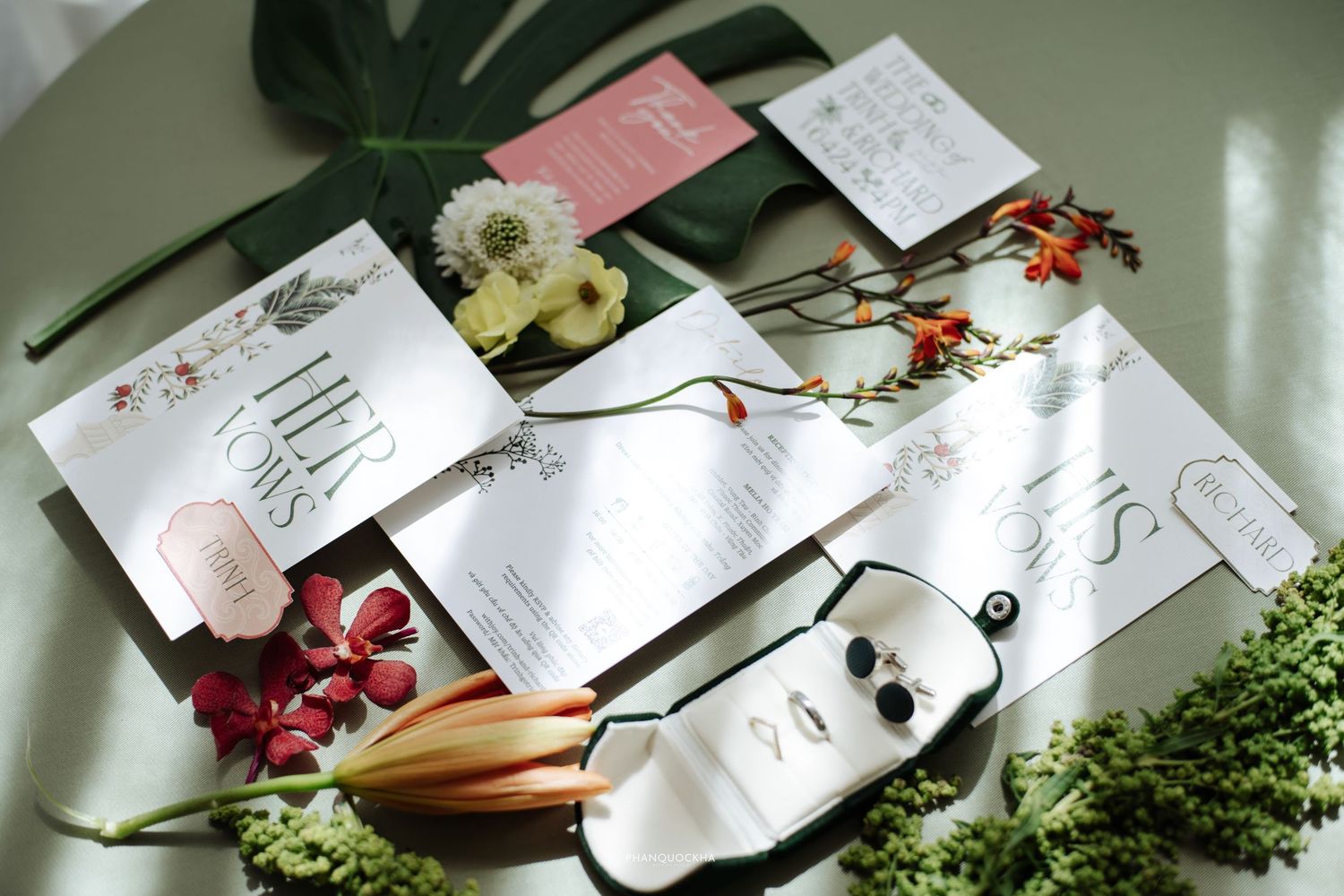 Elegant wedding stationery flat lay with floral arrangements, earrings, and greenery on a light surface.