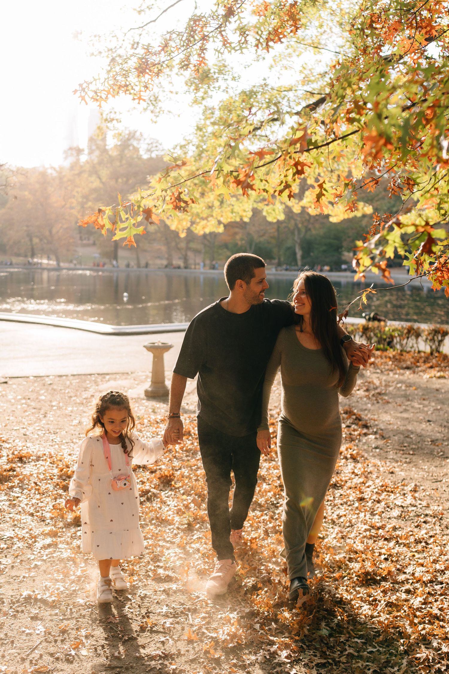Family walking together through autumn leaves on a sunny day while enjoying fall foliage and golden sunlight.