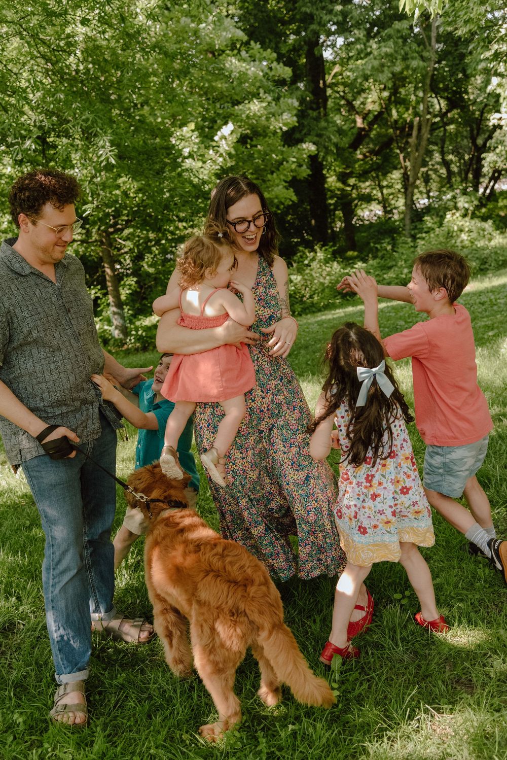 Family with three kids and golden retriever dog playing outdoors in lush green park on sunny day.