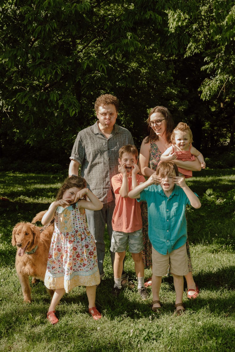 Family of six with a golden retriever posing outdoors on green grass with trees in background.