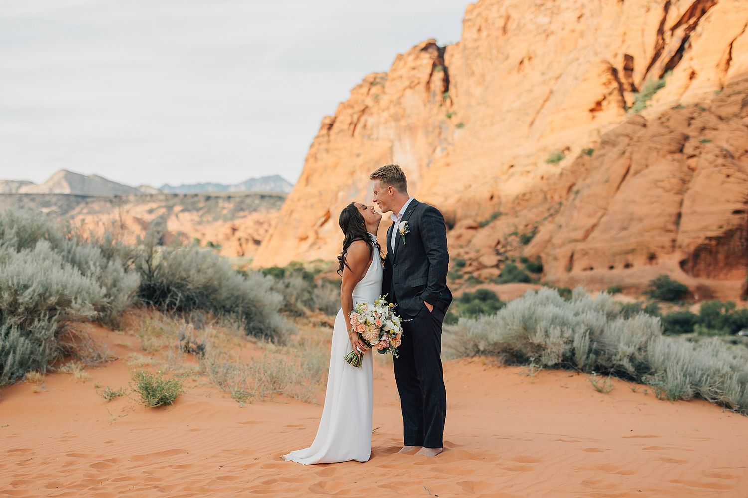 Bride and groom share a romantic kiss in a stunning red rock desert landscape with sandstone formations.