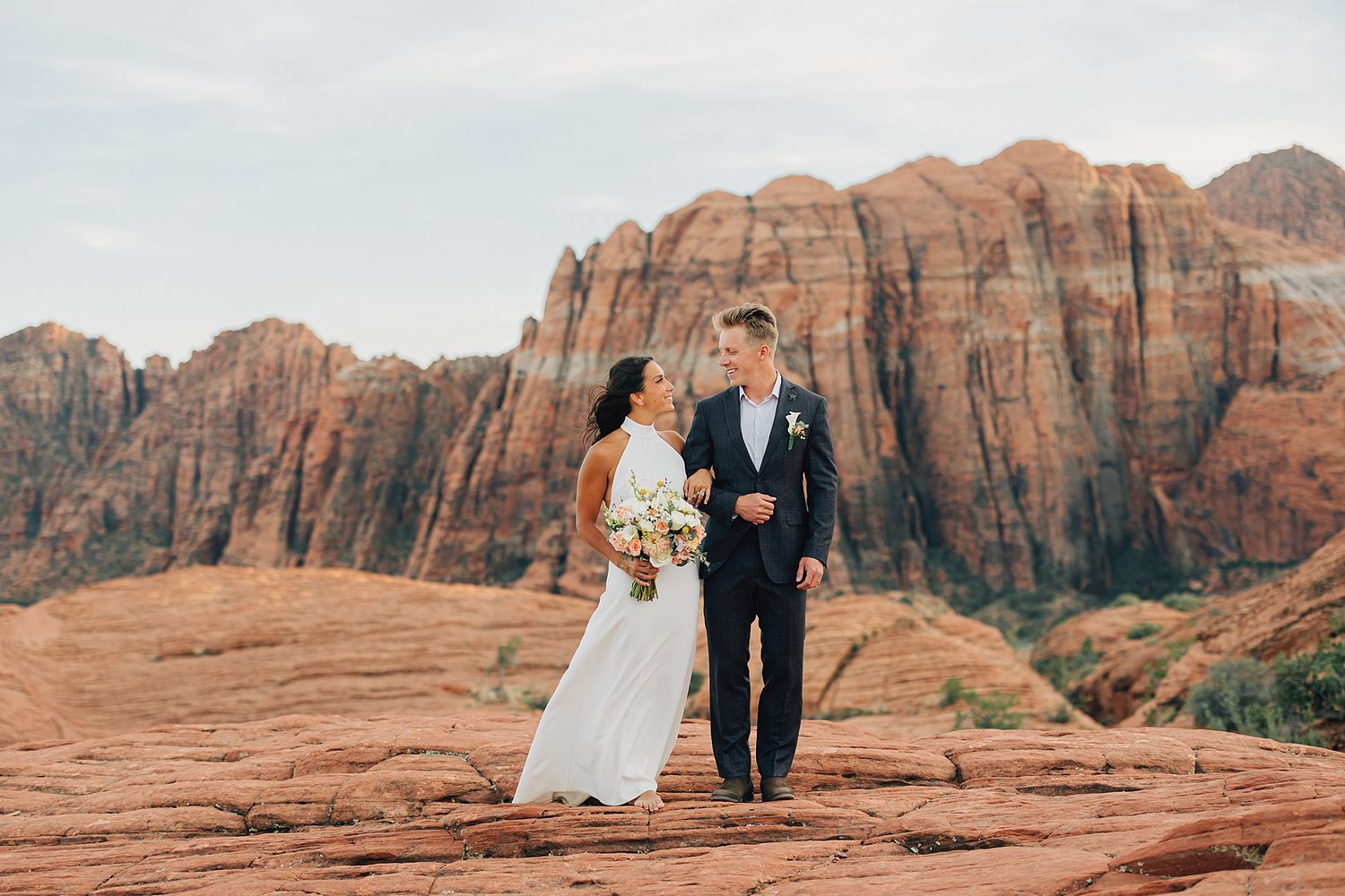 A bride and groom stand on red rock formations with stunning sandstone cliffs backdrop at Zion National Park.