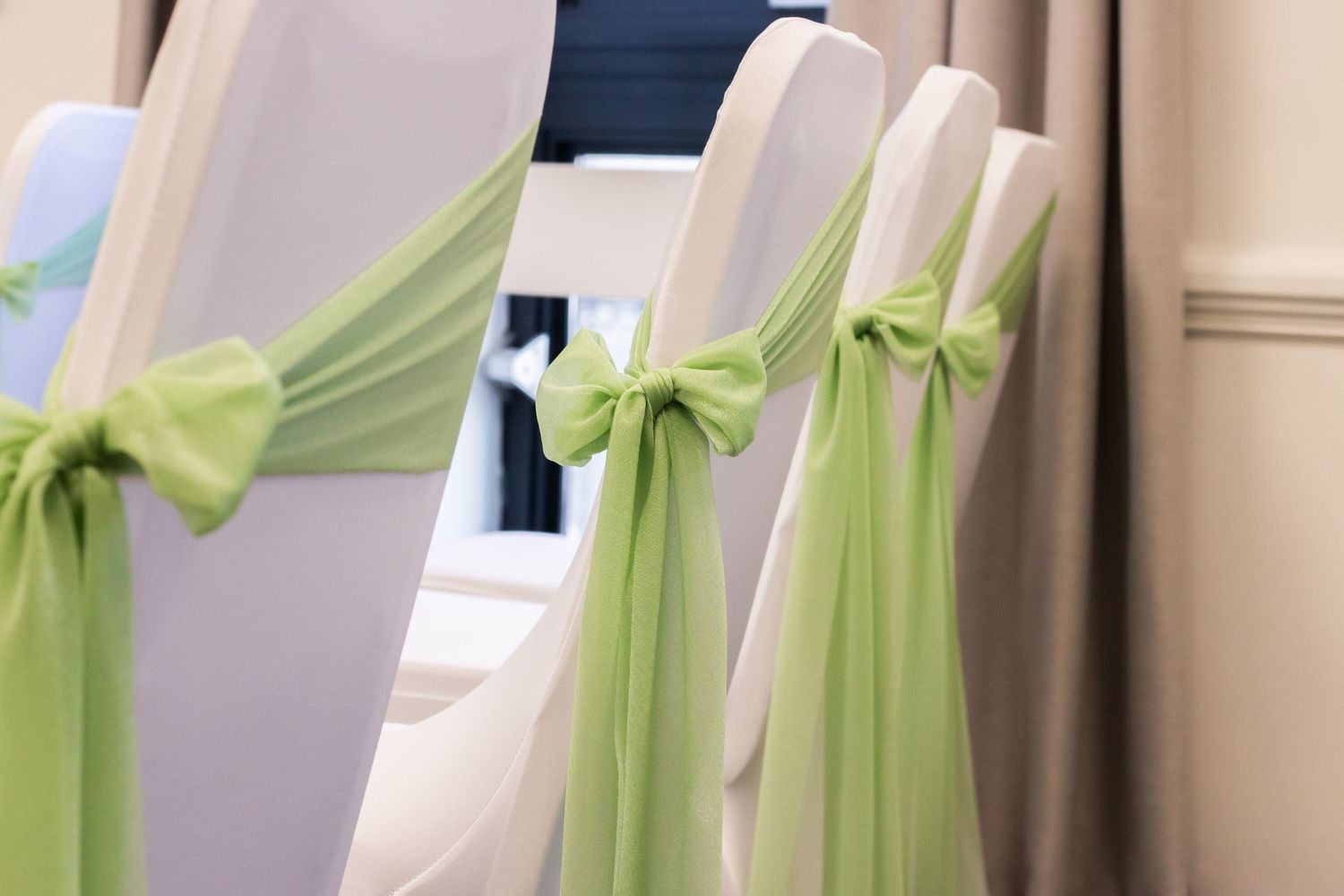 White wedding chairs adorned with elegant lime green satin ribbon bows in a decorated event venue.