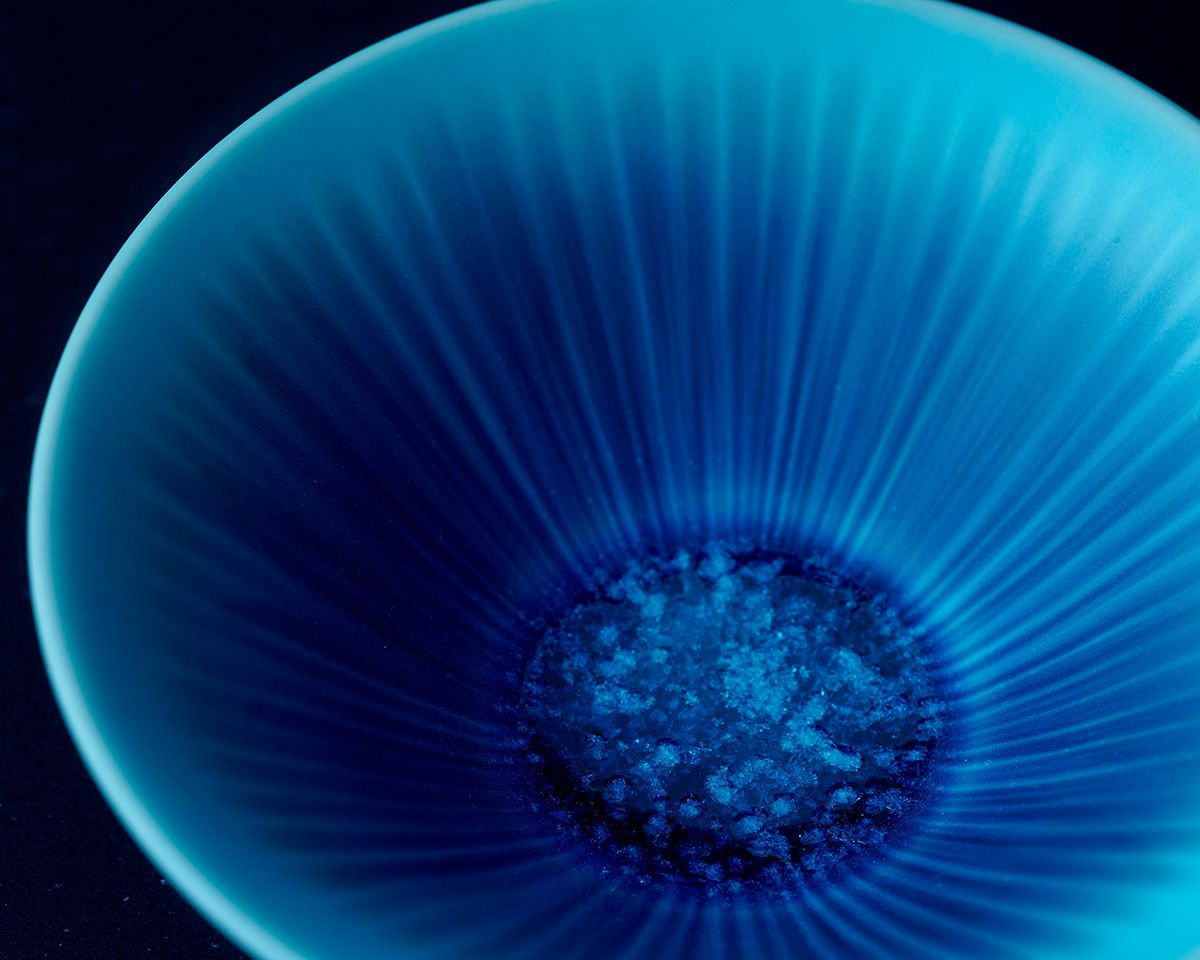 Close-up of a stunning blue ceramic bowl with radiant ribbed texture and intricate crystalline glaze center on dark background.