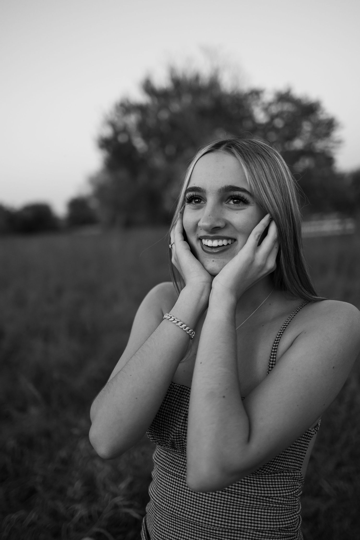 Sioux City, Iowa photographer. Black and white portrait of a smiling young woman with hands on cheeks in a field.