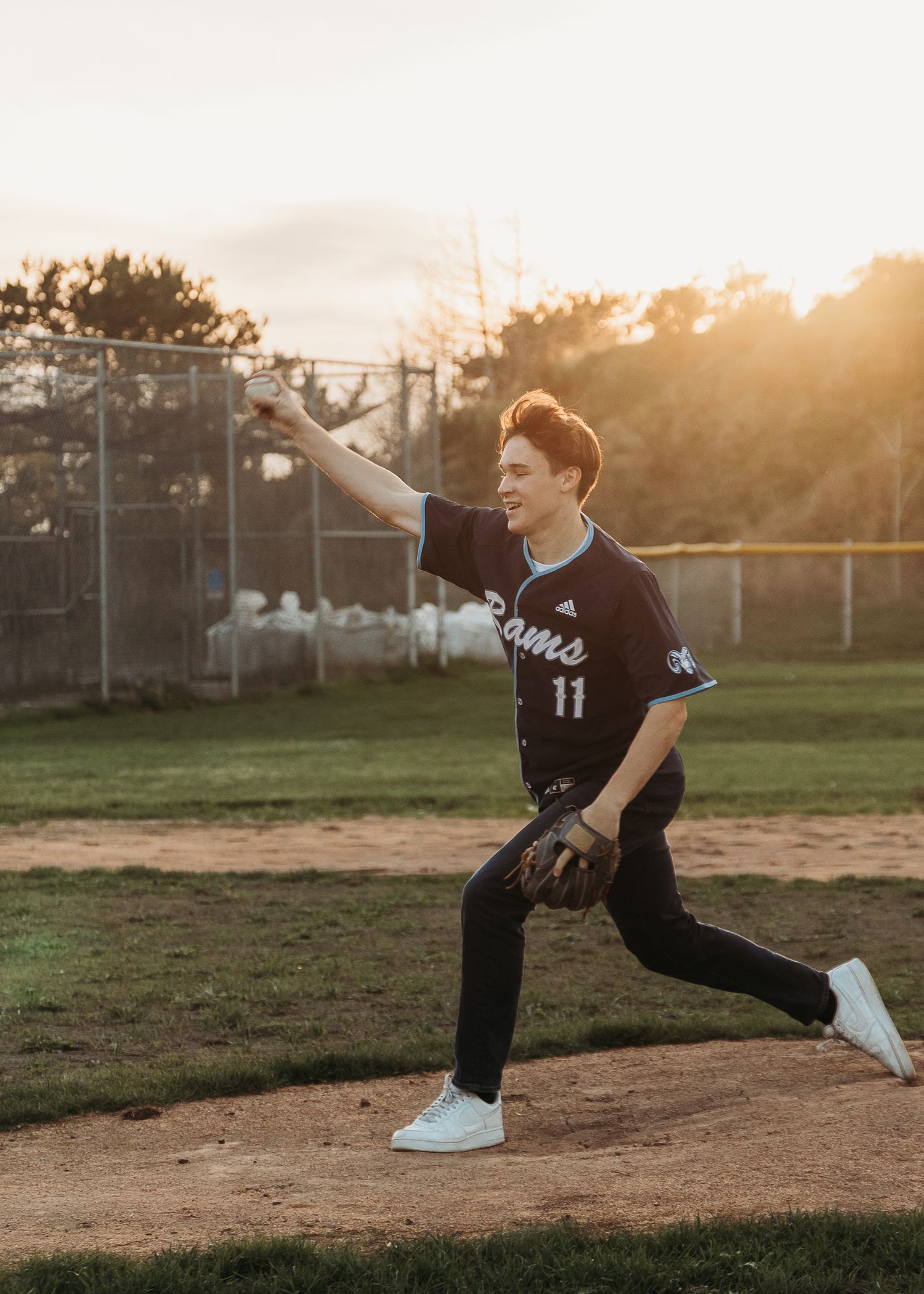 Baseball player wearing jersey number 11 pitching on a sunlit field at golden hour.