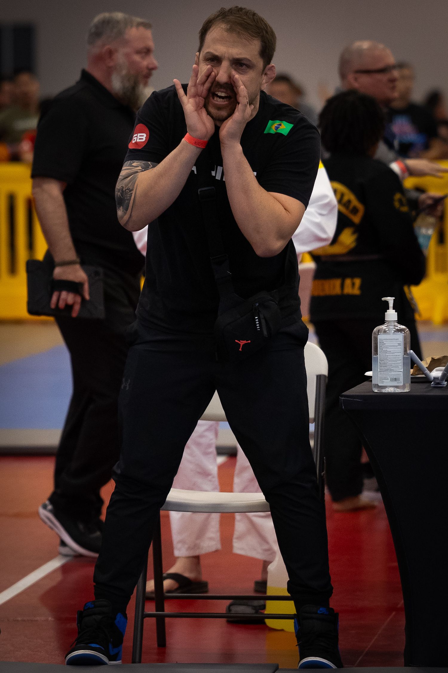 A coach shouts instructions with hands cupped around mouth at a martial arts competition.