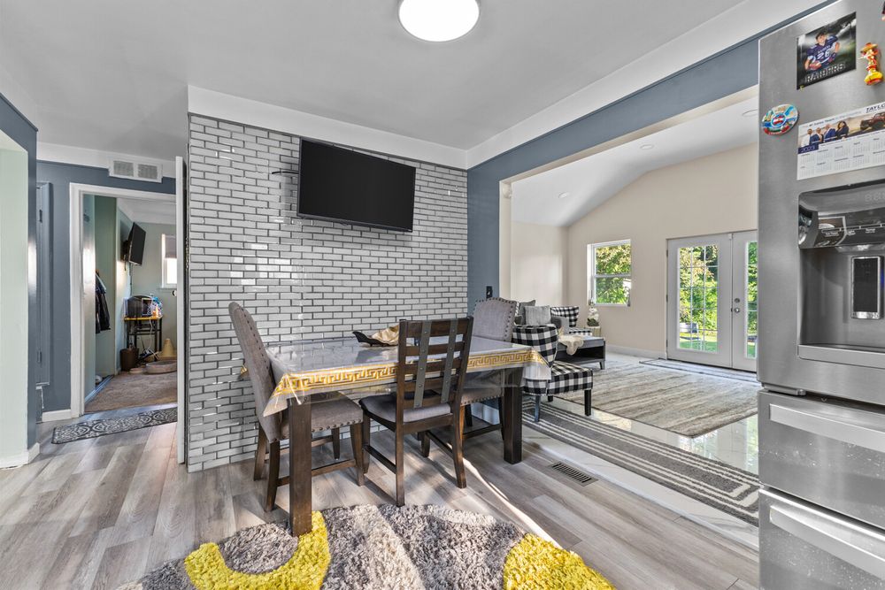 Dining area with exposed brick accent wall, mounted TV, hardwood floors, and vaulted ceiling.