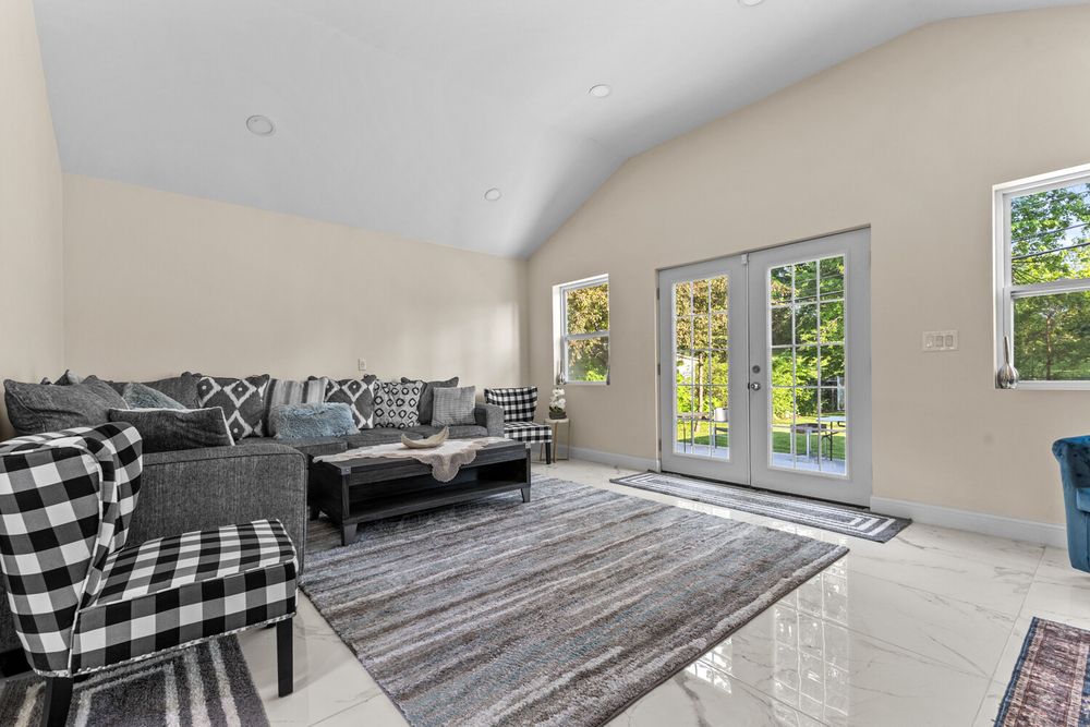 Bright living room with vaulted ceiling, gray sectional sofa, French doors, and large windows.
