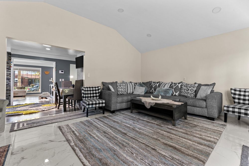 Open-concept living and dining area with gray sectional, brick accent wall, and vaulted ceiling.