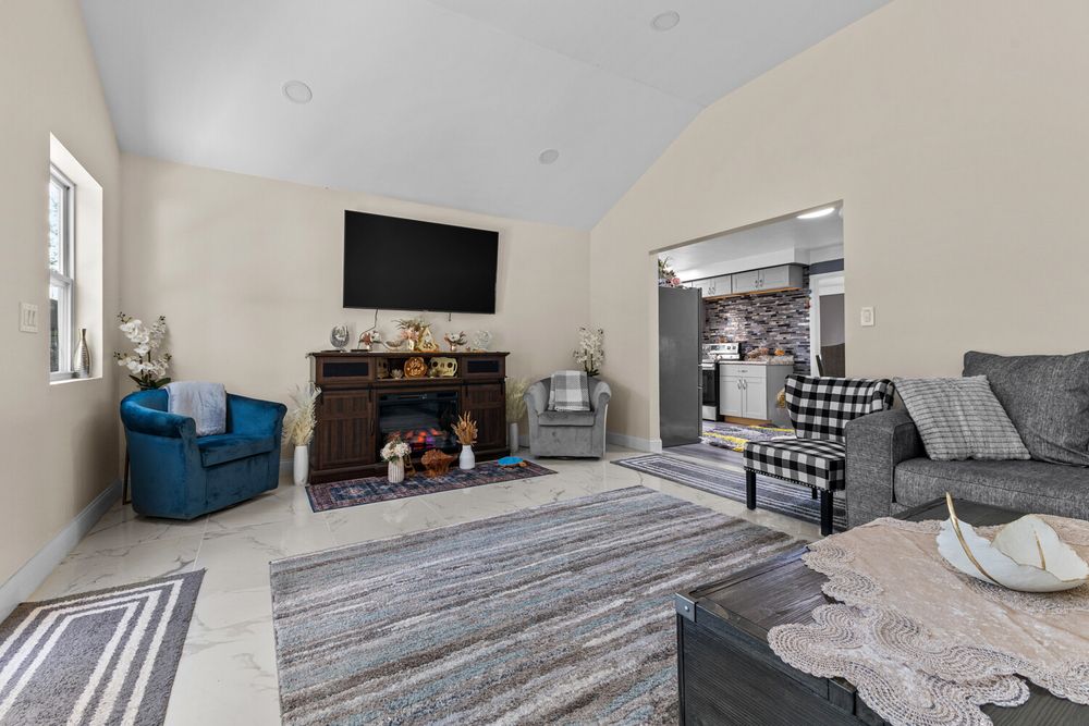Living room with vaulted ceiling, wall-mounted TV, fireplace, blue accent chair, and gray sofa.