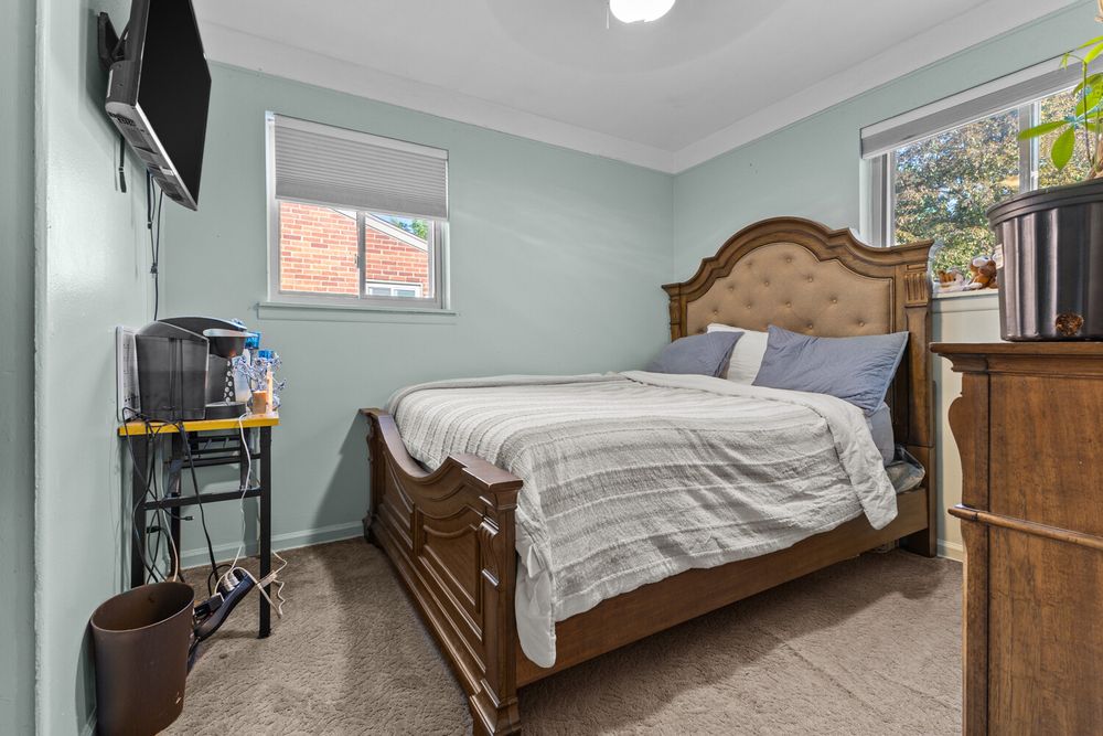 Cozy bedroom with wooden sleigh bed, carpeted floors, wall-mounted TV, and light blue walls with crown molding.