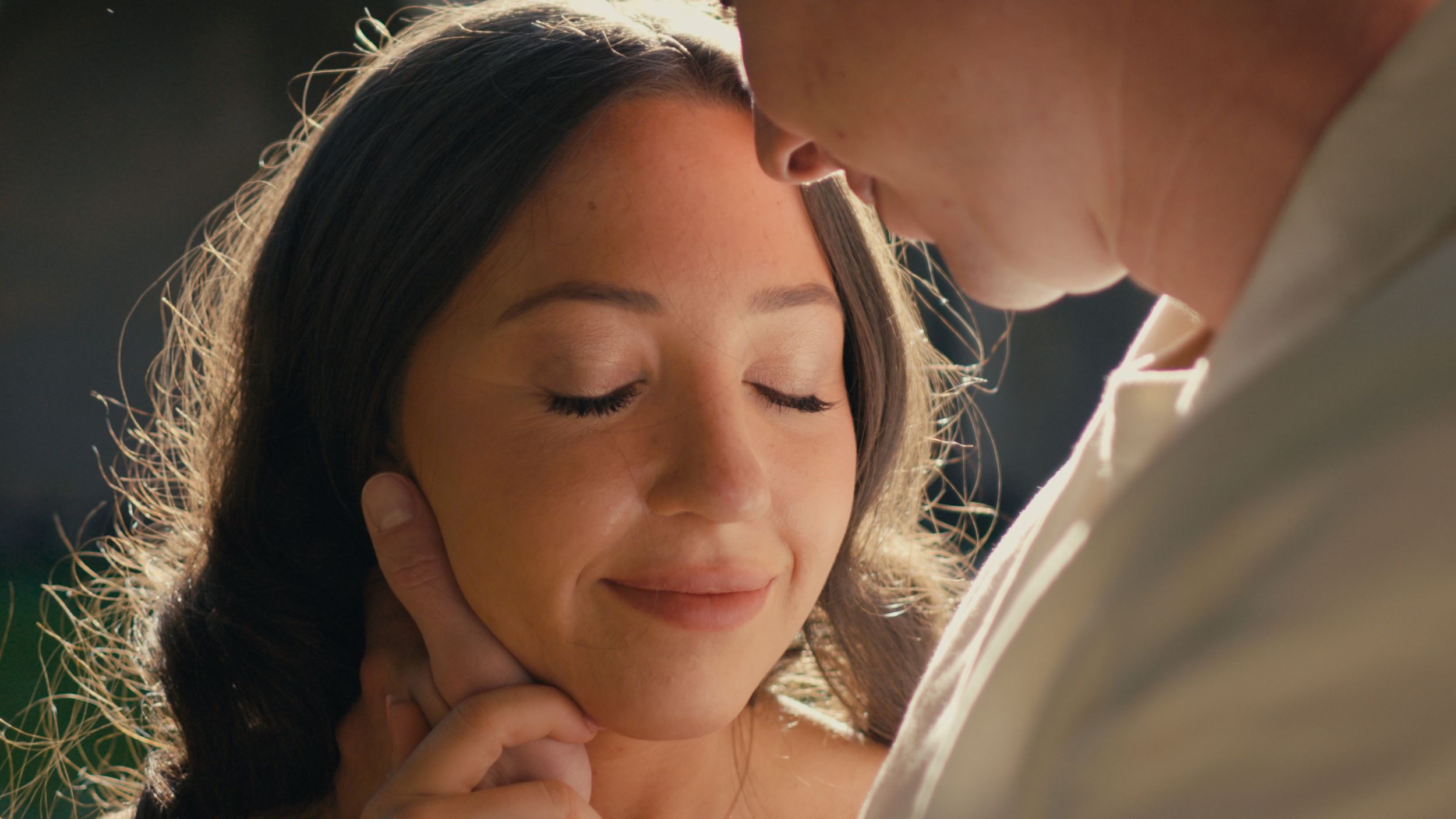 A romantic couple sharing an intimate moment, woman smiling with eyes closed as man tenderly touches her face.