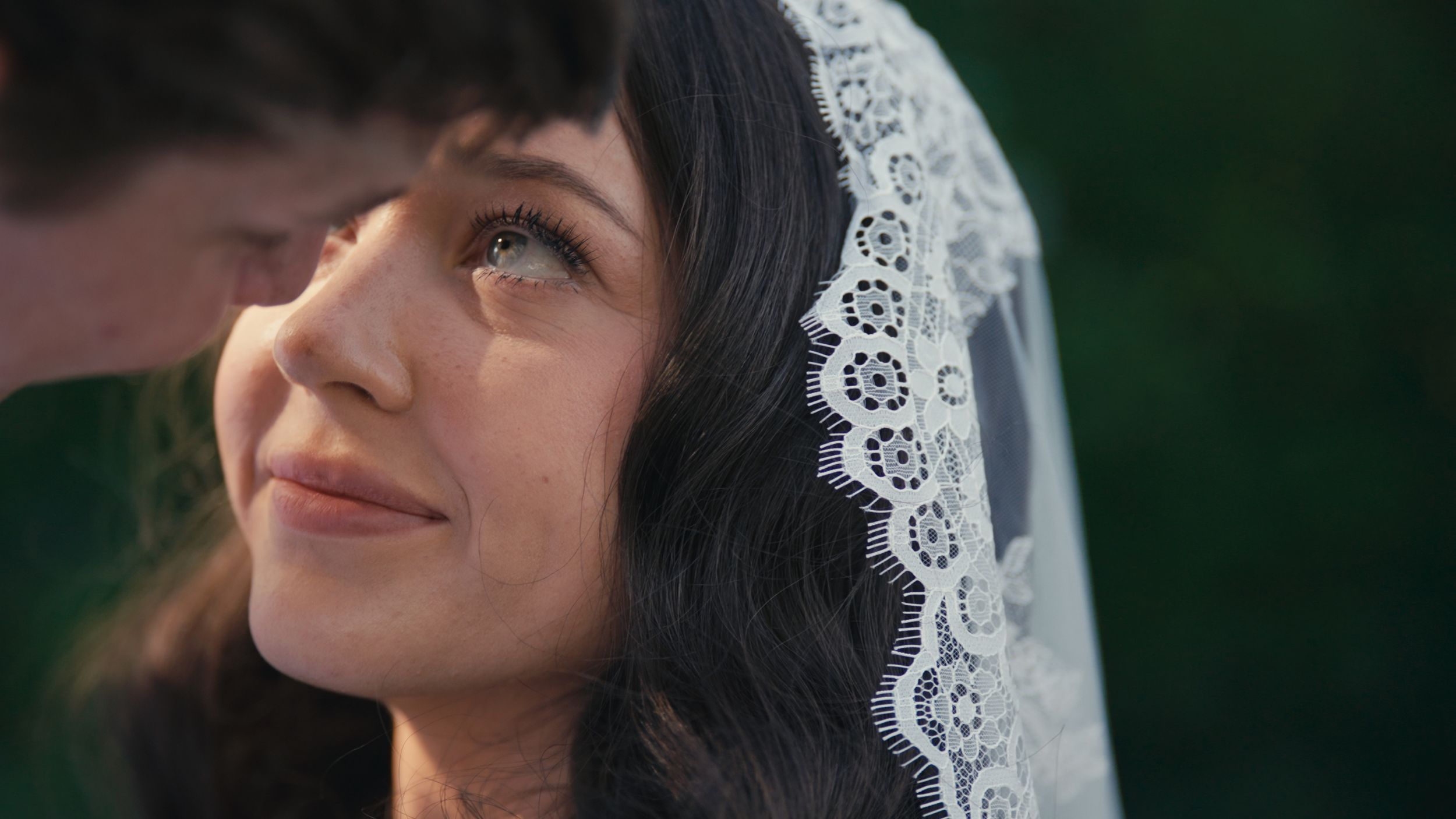 Bride wearing lace veil looks up emotionally on her wedding day, tears in her eyes.