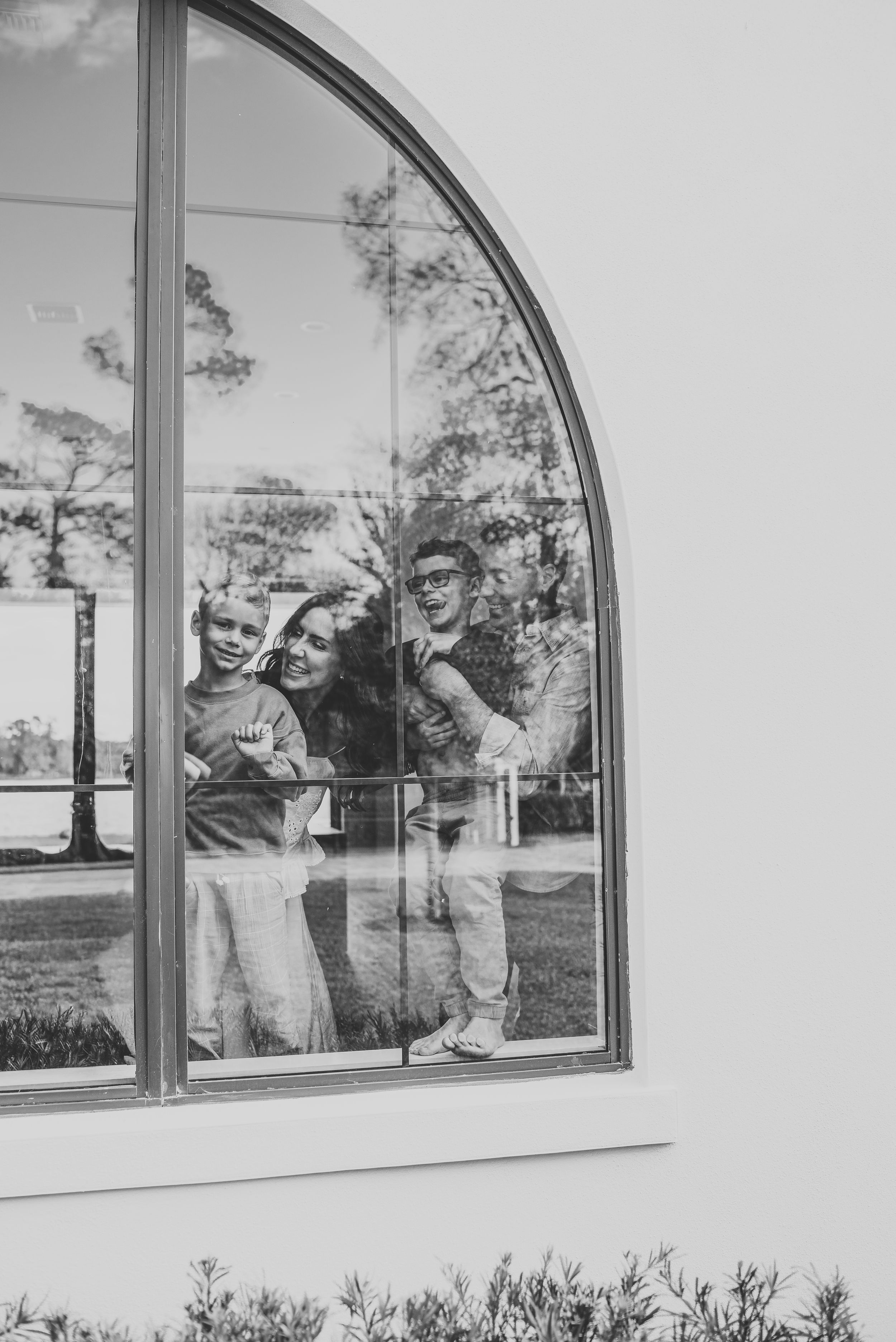 In-home lifestyle photography with a family of three smiling through an arched window of a white building in orlando Florida.