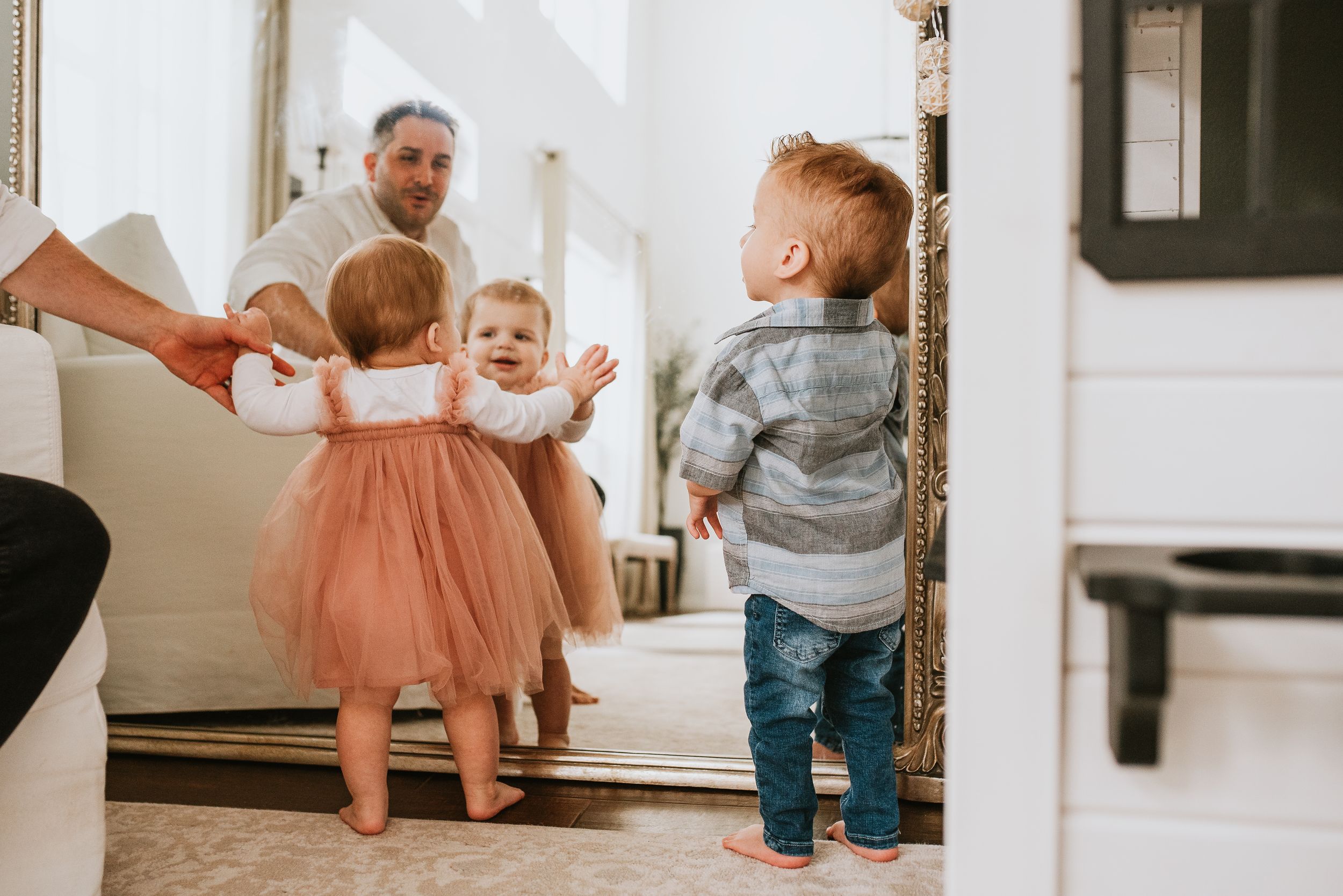 A man sits on a couch watching two toddlers play together in a bright, cozy living room during an orlando in-home photography session.