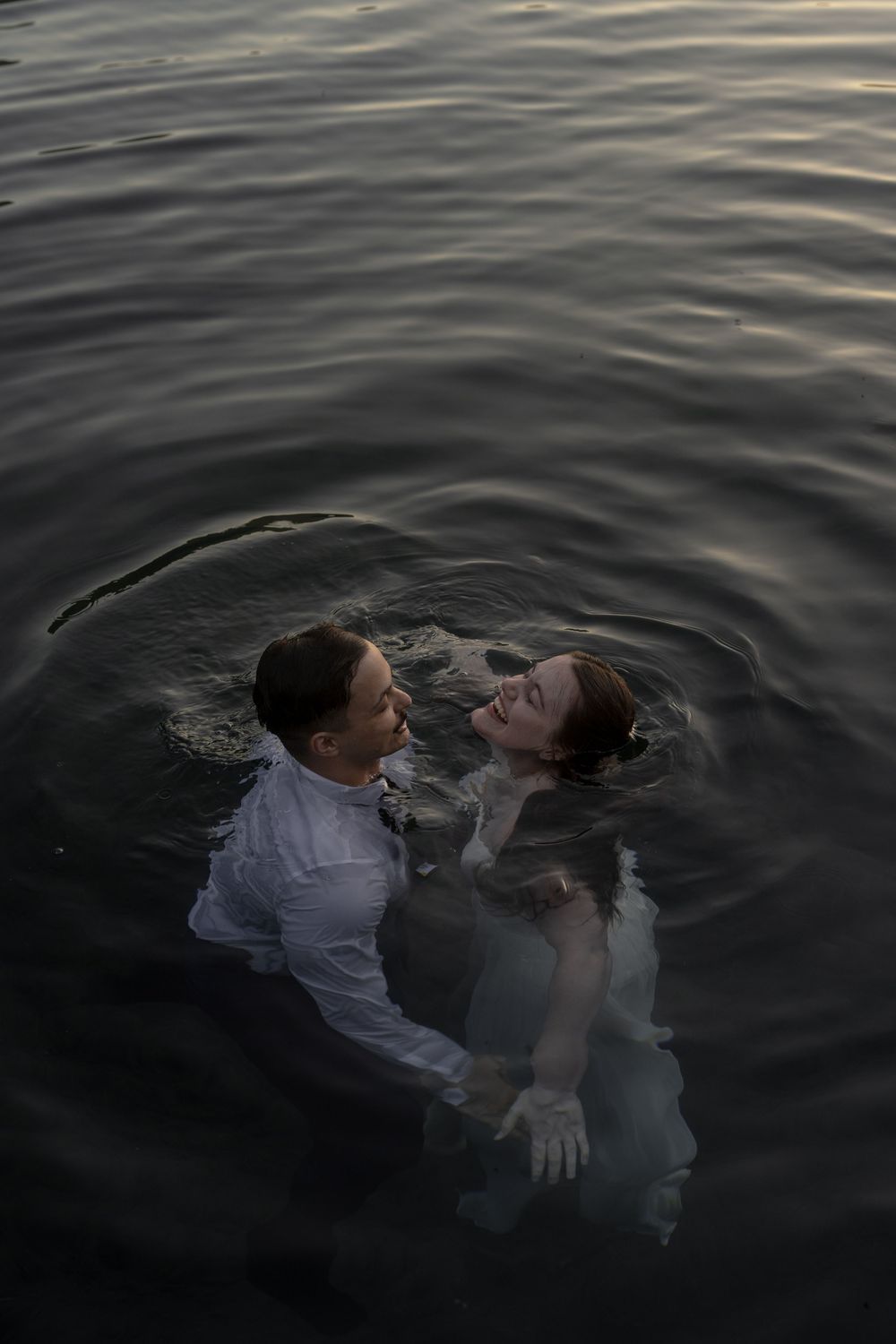 Couple embracing romantically in dark water during an outdoor wedding photo shoot at dusk.