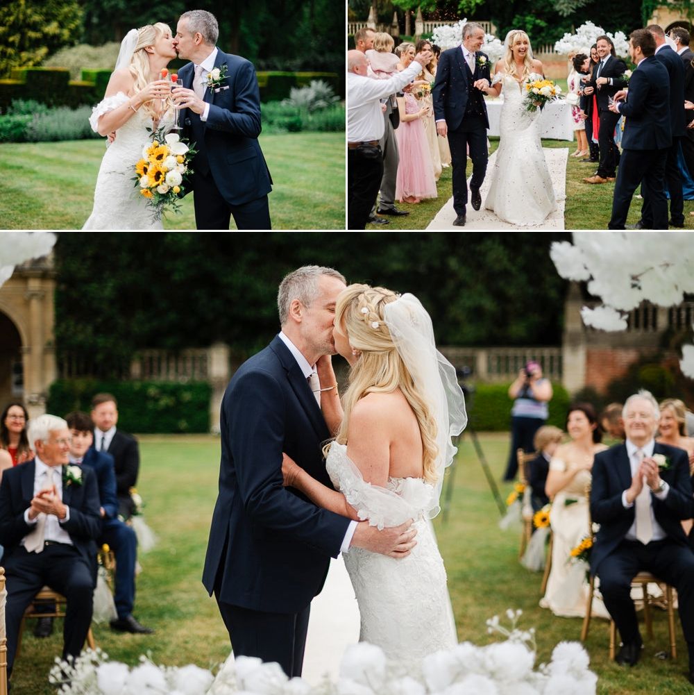 Outdoor wedding ceremony with bride and groom kissing, guests applauding, surrounded by lush greenery and sunflower bouquets.