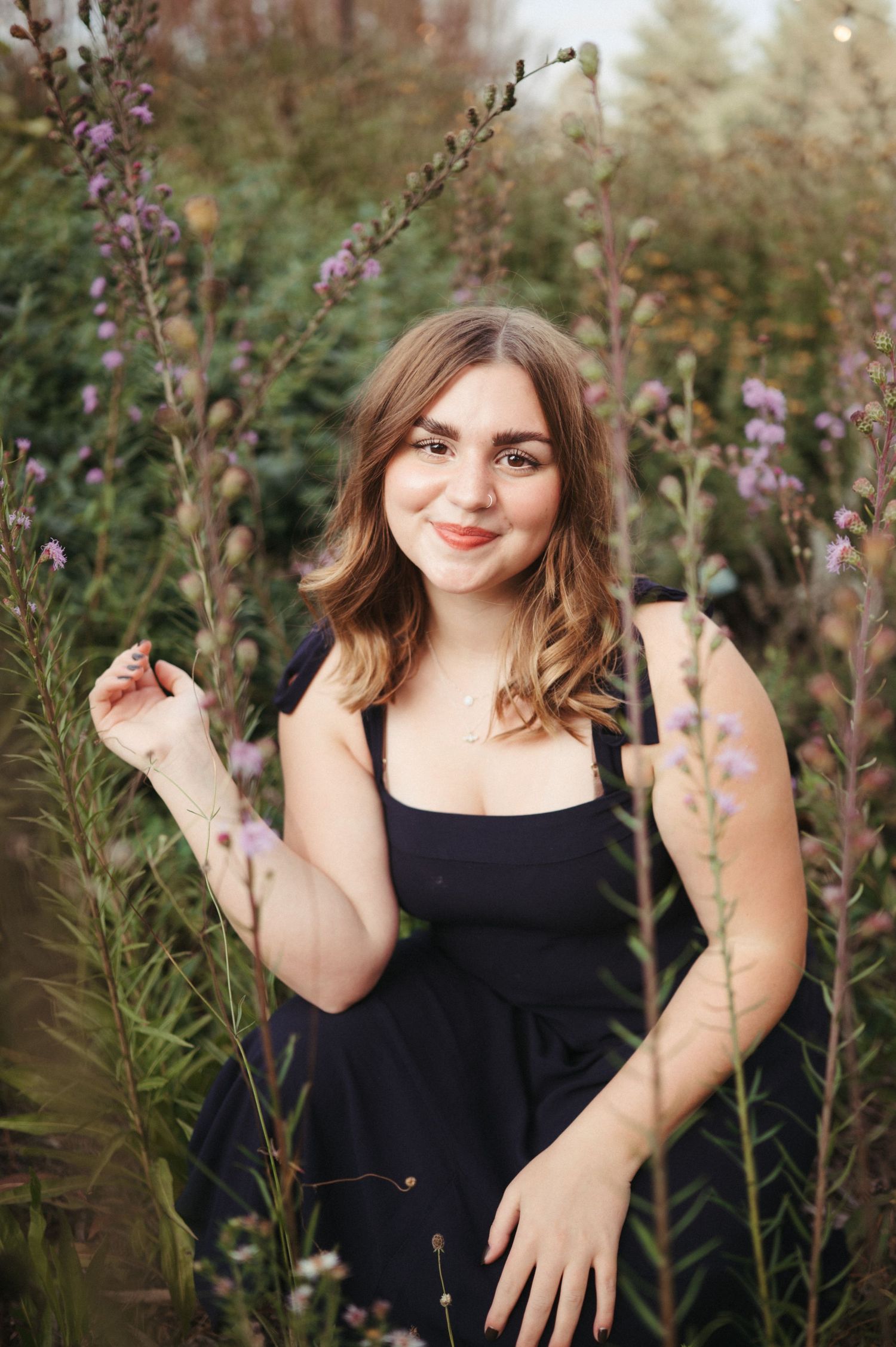Senior girl in a navy blue dress photographed in lush greenery with warm golden light and a timeless outdoor feel.