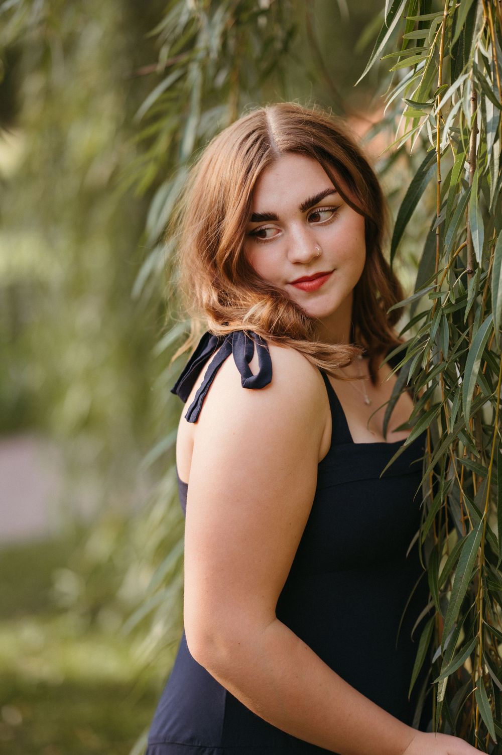 Natural light senior girl portrait with dark greenery, soft warmth and a classic film-inspired feel.