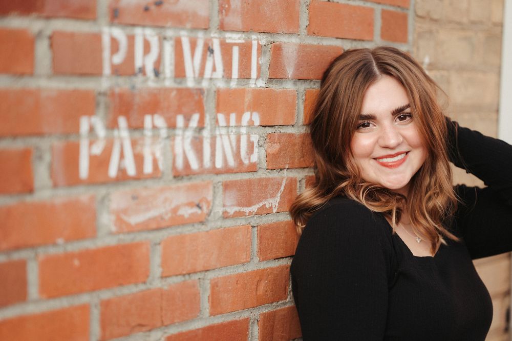 Senior girl in a urban setting setting with brick wall, soft warmth and clean timeless edits.