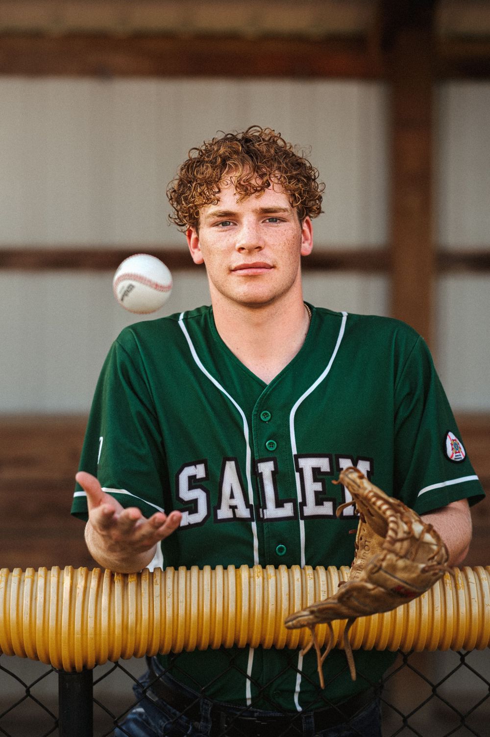 Outdoor senior boy with rich green jersey, subtle grain and a tossing a baseball.