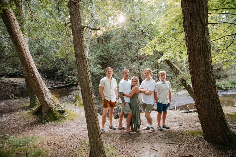 Family of five posing together in a lush forest setting with trees and a stream in the background.