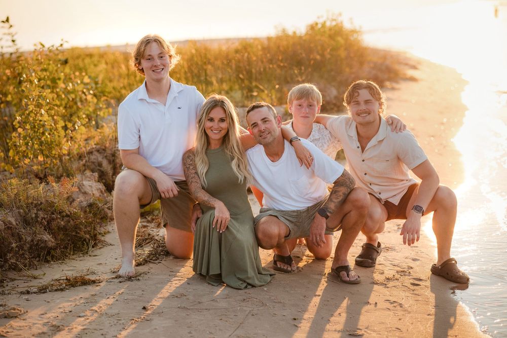 Happy family of five posing together on a sandy beach path during golden hour sunset.
