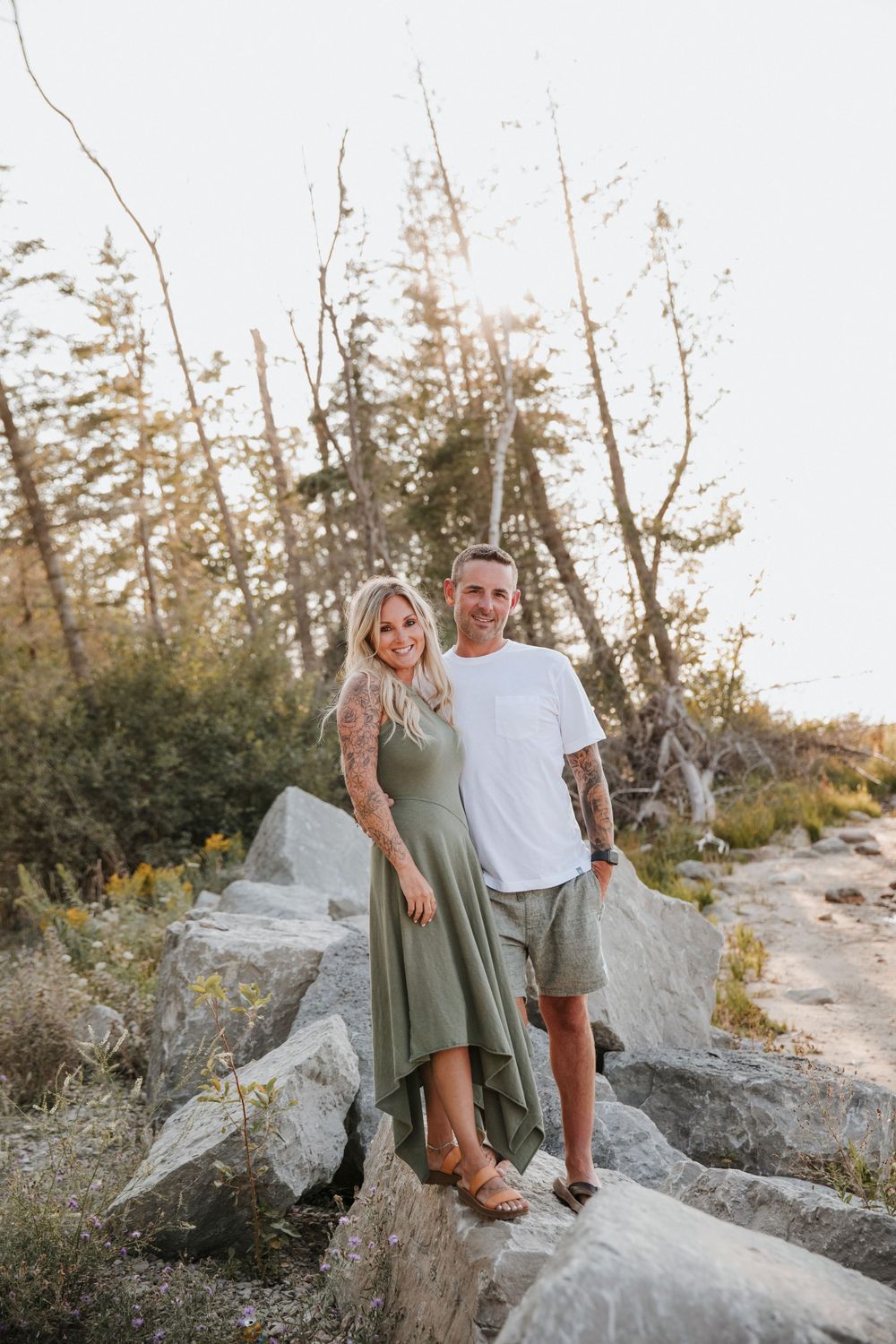 Smiling couple standing on large rocks surrounded by trees in warm golden light.