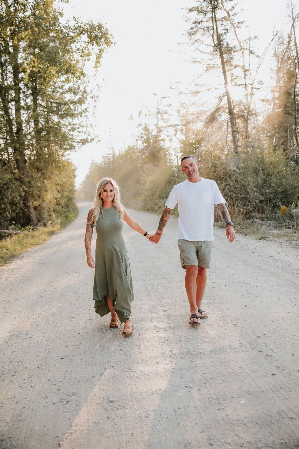 Couple holding hands walking on a sunny dirt road surrounded by trees in Northern Michigan